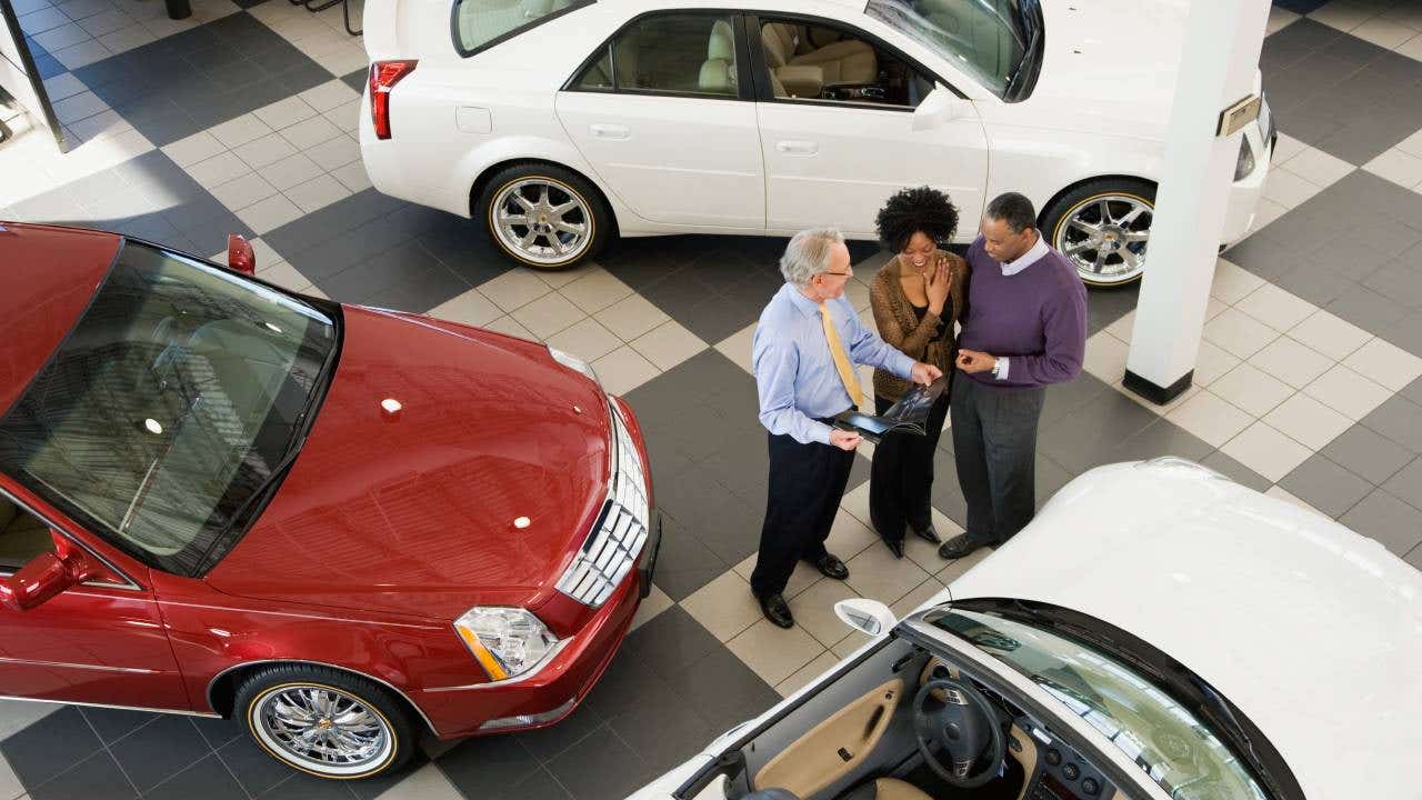 A Black couple talk to a salesperson at a car dealership.