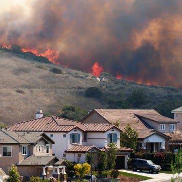 A suburban neighborhood near a hill with a wildfire in the background.