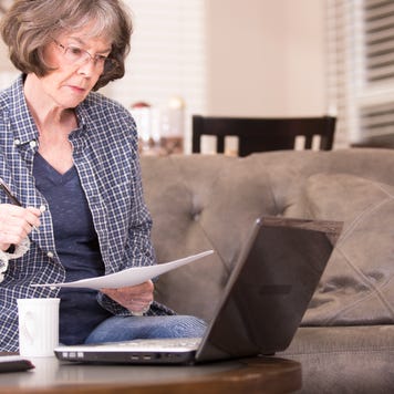 Older woman reviews financial documents and has a laptop.