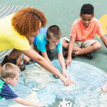 A teacher and children drawing the globe in chalk