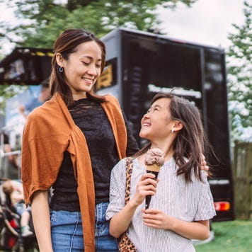 Lovely girl enjoying ice cream with her young pretty mom in front of a food truck at food festival