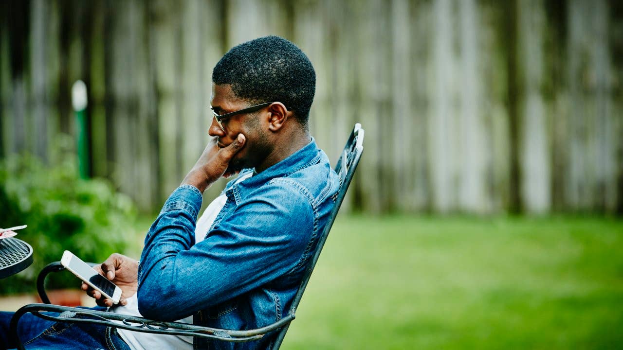 Man seated in backyard checking smartphone.