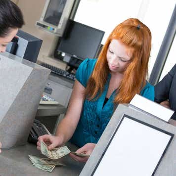 Young bank teller counting money as her supervisor watches