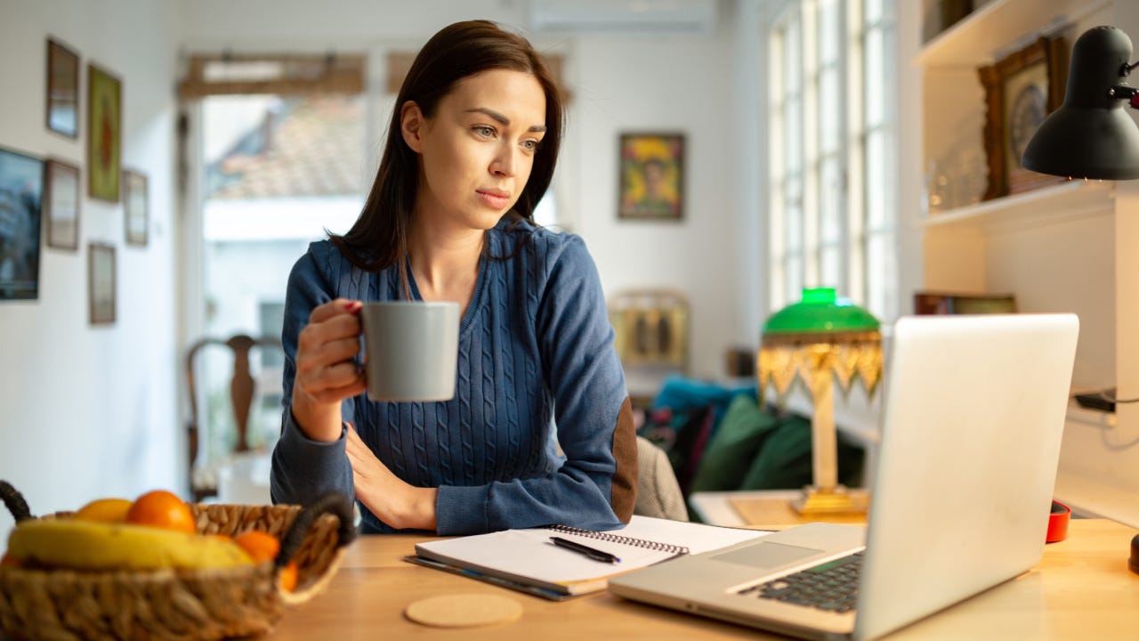 young woman sitting in her living room, working from home using her laptop