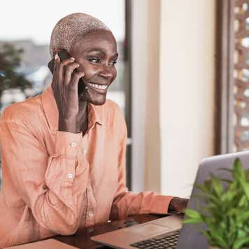woman working with laptop outdoor while talking on smartphone call