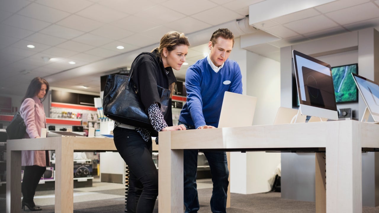 Salesman assisting female customer in buying laptop at store