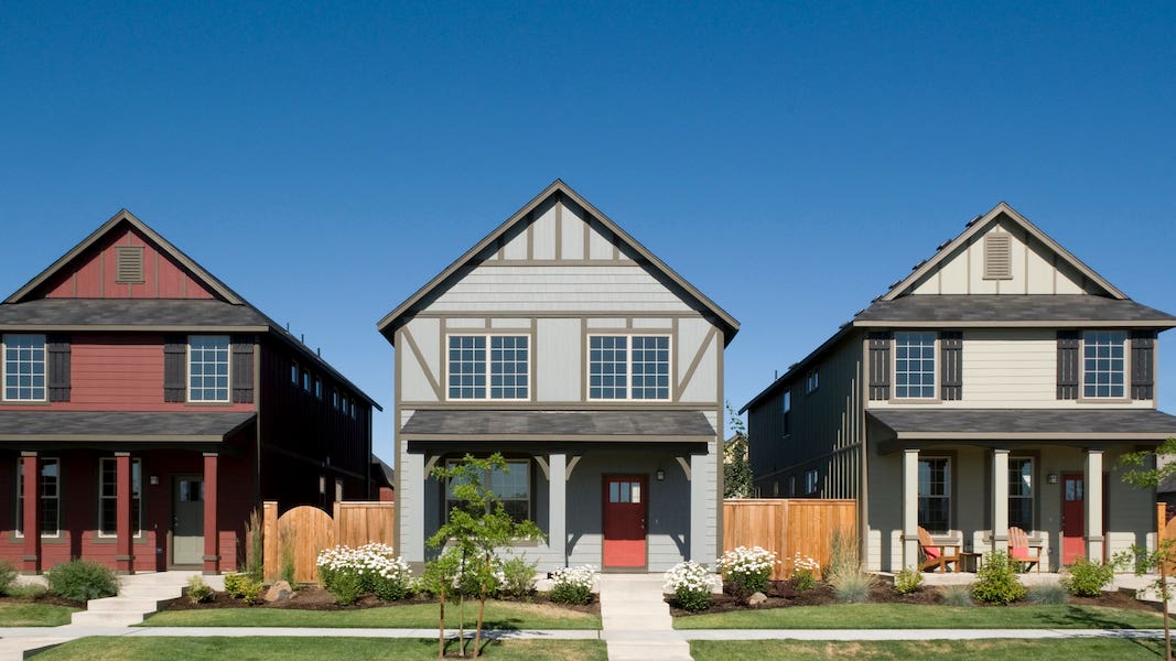 three modest suburban homes with front porches and blue sky