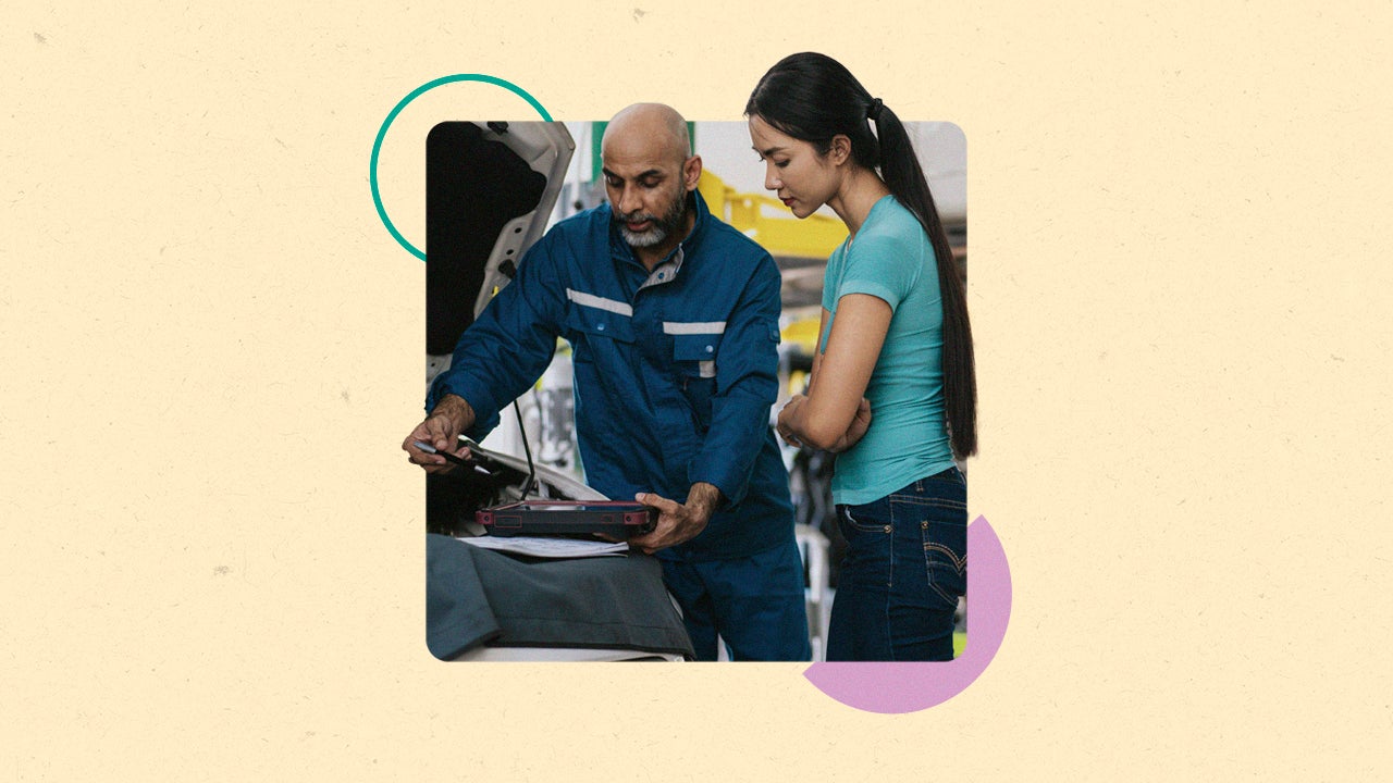 A young Asian woman and a Black mechanic look at the engine of a car.
