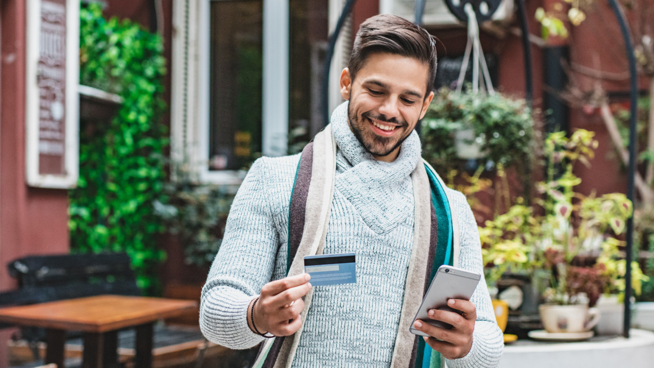 A young man in warm clothing using a mobile phone and credit card