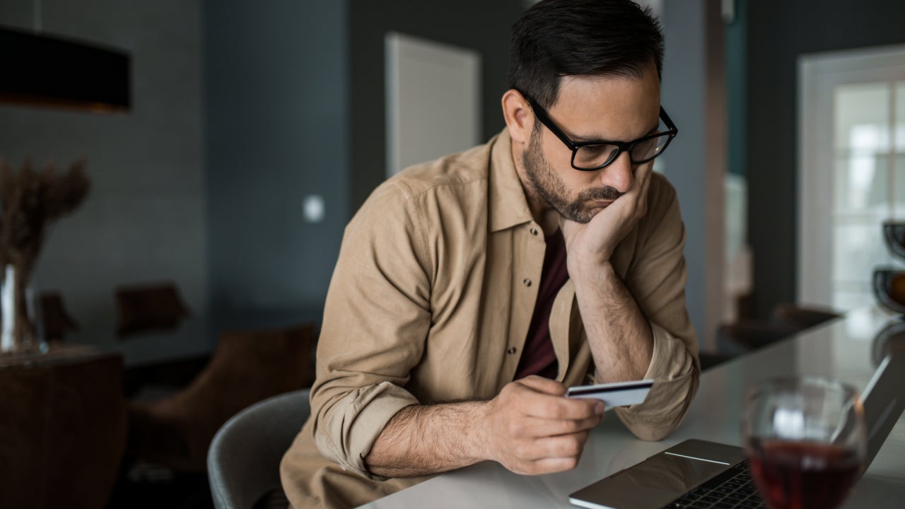 Young entrepreneur paying online with credit card on his laptop at home and going bankrupt.