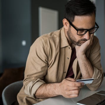 Young entrepreneur paying online with credit card on his laptop at home and going bankrupt.
