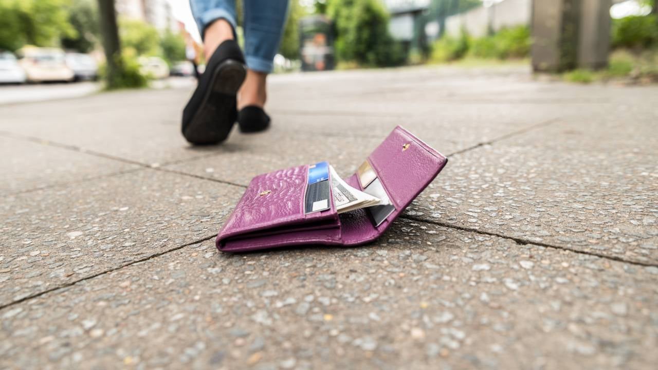 Ground-level shot of a wallet with credit cards on the ground and person walking away.