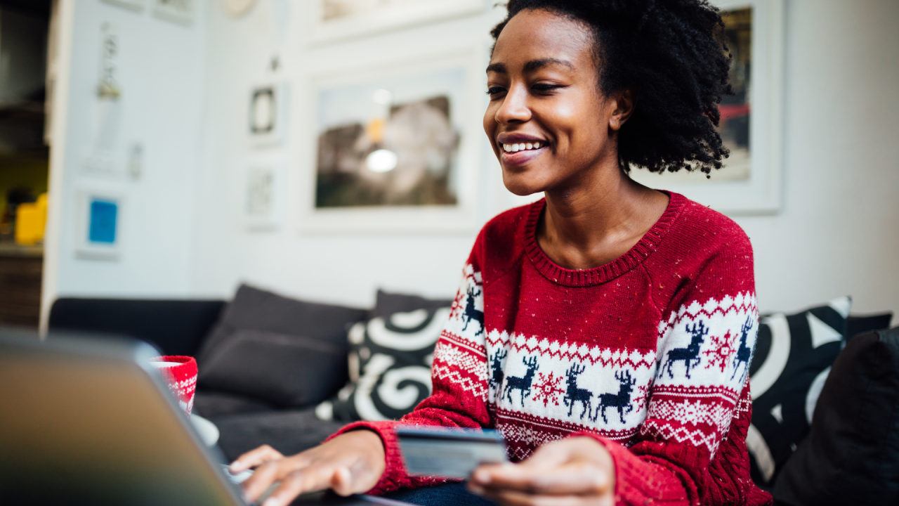 Beautiful African American woman shopping online from her cozy home office during winter holidays, holding a credit card while purchasing something online using a laptop