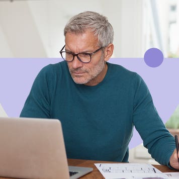 Older white man uses a laptop while writing on a piece of paper.