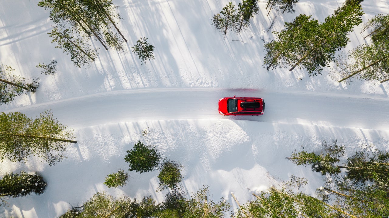 Aerial view of a red car driving through a snowy forest.