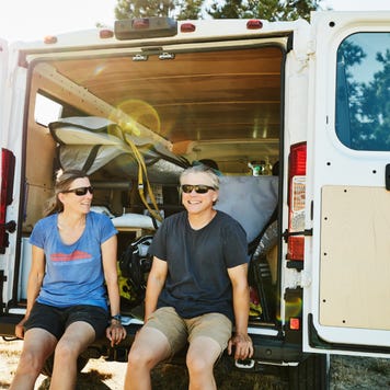 Smiling couple sitting on back of van after windsurfing on summer afternoon