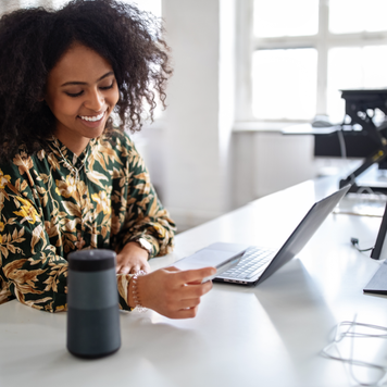 Woman with a credit card talking into a smart assistance device to do a online payment. Woman using wireless technology for online shopping.
