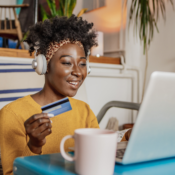 A young woman is in the living room, she is using a laptop and credit card