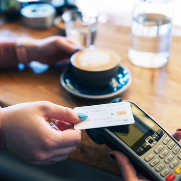 Clsoe-up of unrecognisable woman making contactless card payment in cafe.