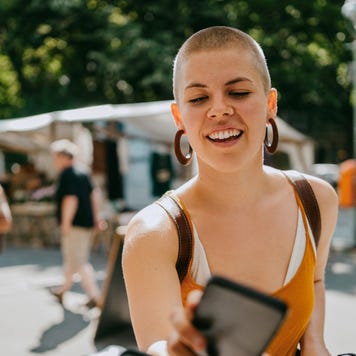 Smiling woman with shaved head paying via tap to pay while shopping at flea market