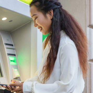 Female Person Using Mobile Phone Banking App While Standing in Front of Atm Cashpoint Machine. Nfc Online Banking Concept