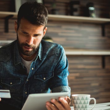 Man holding credit card while using digital tablet in the office.