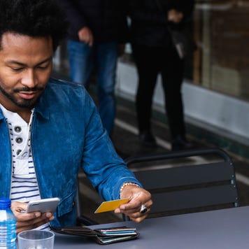 Mid adult man using credit card and smart phone for paying at sidewalk cafe