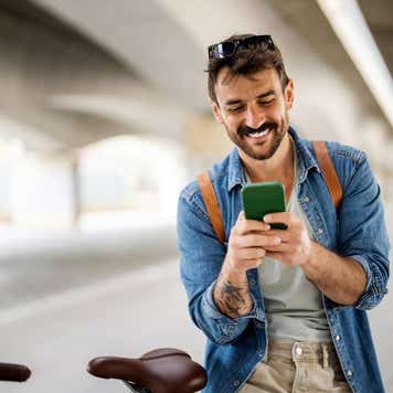 Young man stands next to a bike and smiles at his mobile phone.