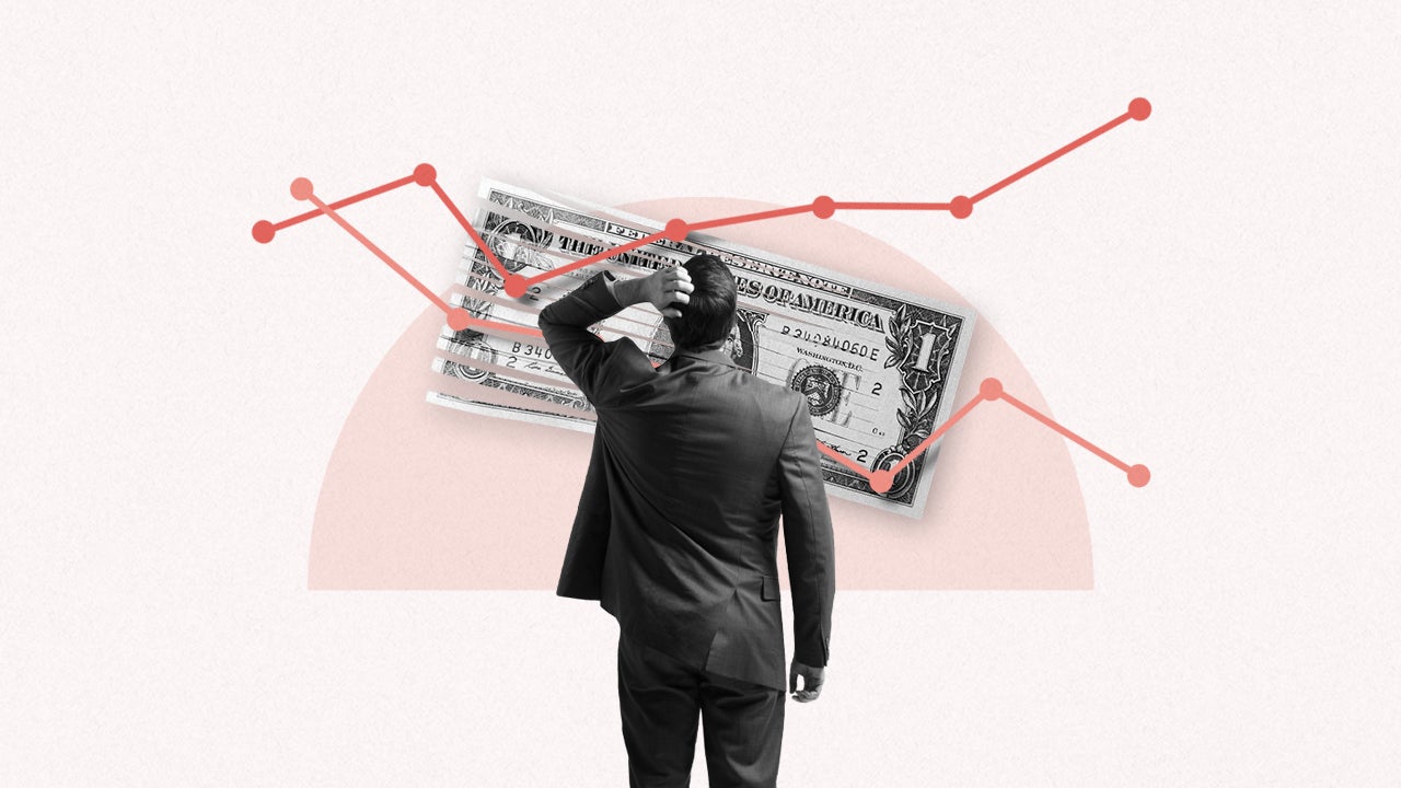 Image of the back of a man in a suit standing in front of a large line graph that is on top of a half shredded U.S. Dollar.