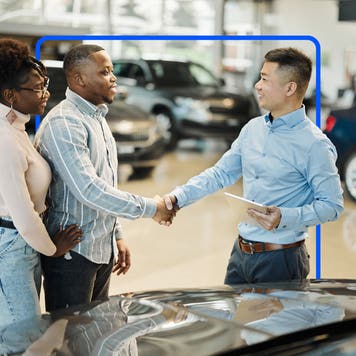 People looking at car and shaking hands while smiling