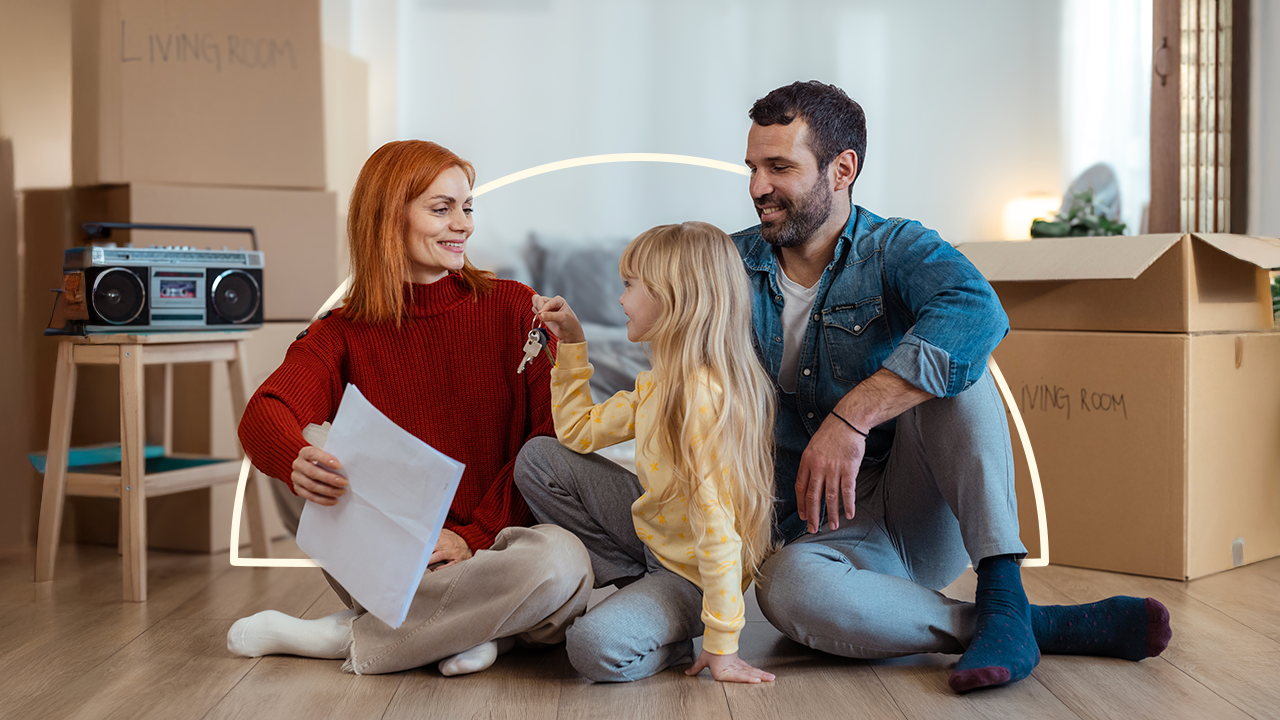 happy couple sitting on floor with young daughter who is holding keys to their new home