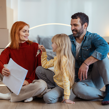 happy couple sitting on floor with young daughter who is holding keys to their new home