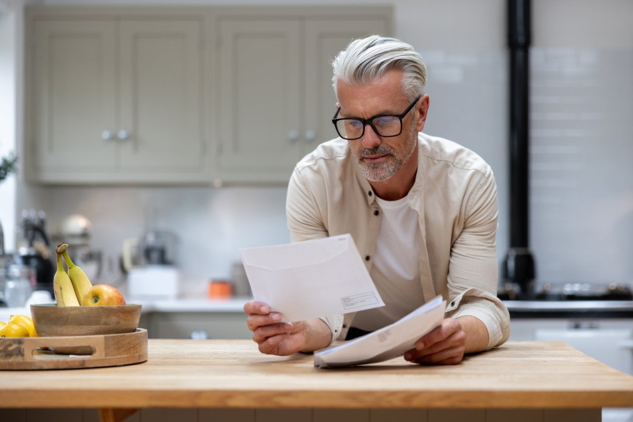 Man at home reading a letter he got in his mail at the kitchen – lifestyle concepts