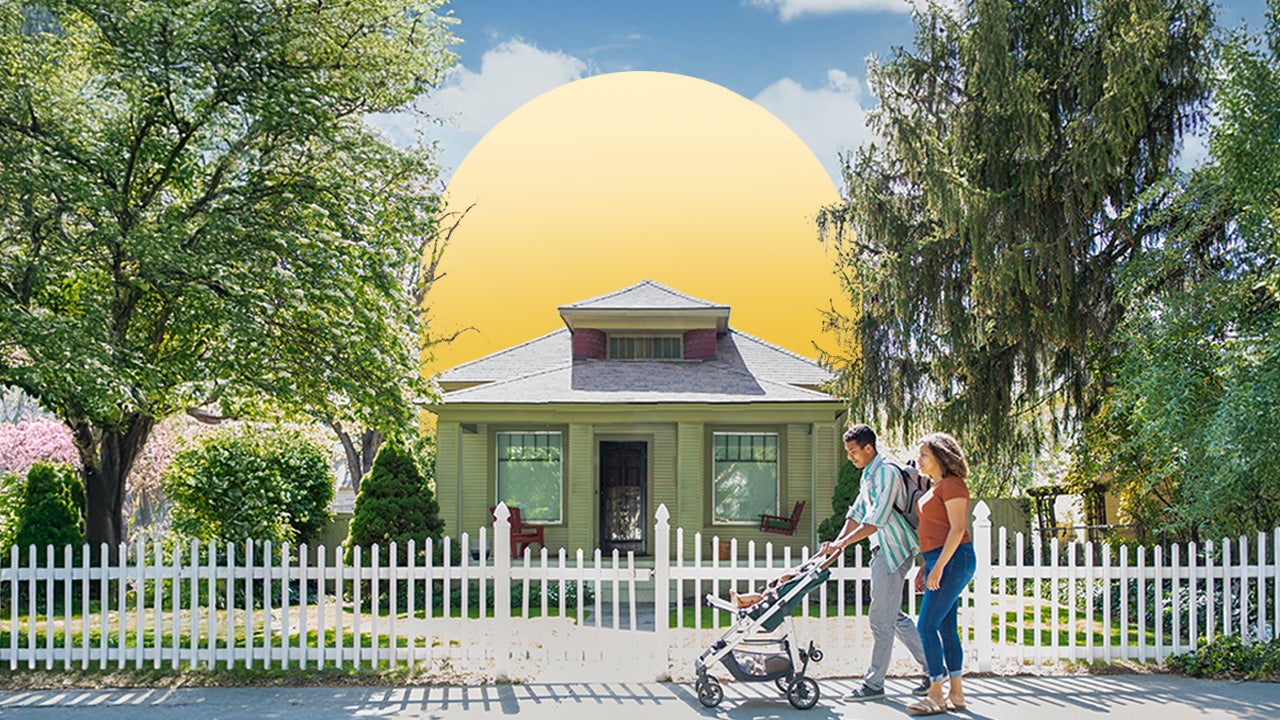 couple walking with baby stroller in front of house with white picket fence