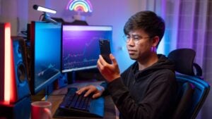 A young man trades crypto in his home office on his smartphone.