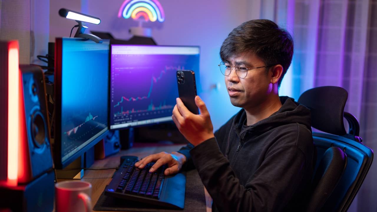 A young man trades crypto in his home office on his smartphone.