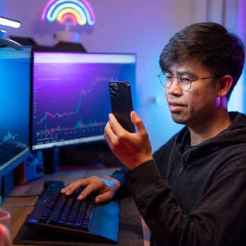 A young man trades crypto in his home office on his smartphone.