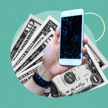 Close up of a hand holding a smartphone with a cracked screen against a background of dollar bills