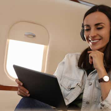 Young woman with tablet and headphones listening to music in airplane during flight