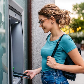 Young woman withdrawing money using phone at the ATM machine on the street in Budapest in Hungary.