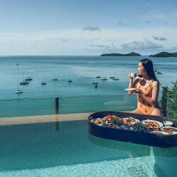 A woman drinking coffee and breakfast floating on the water beside the pool.