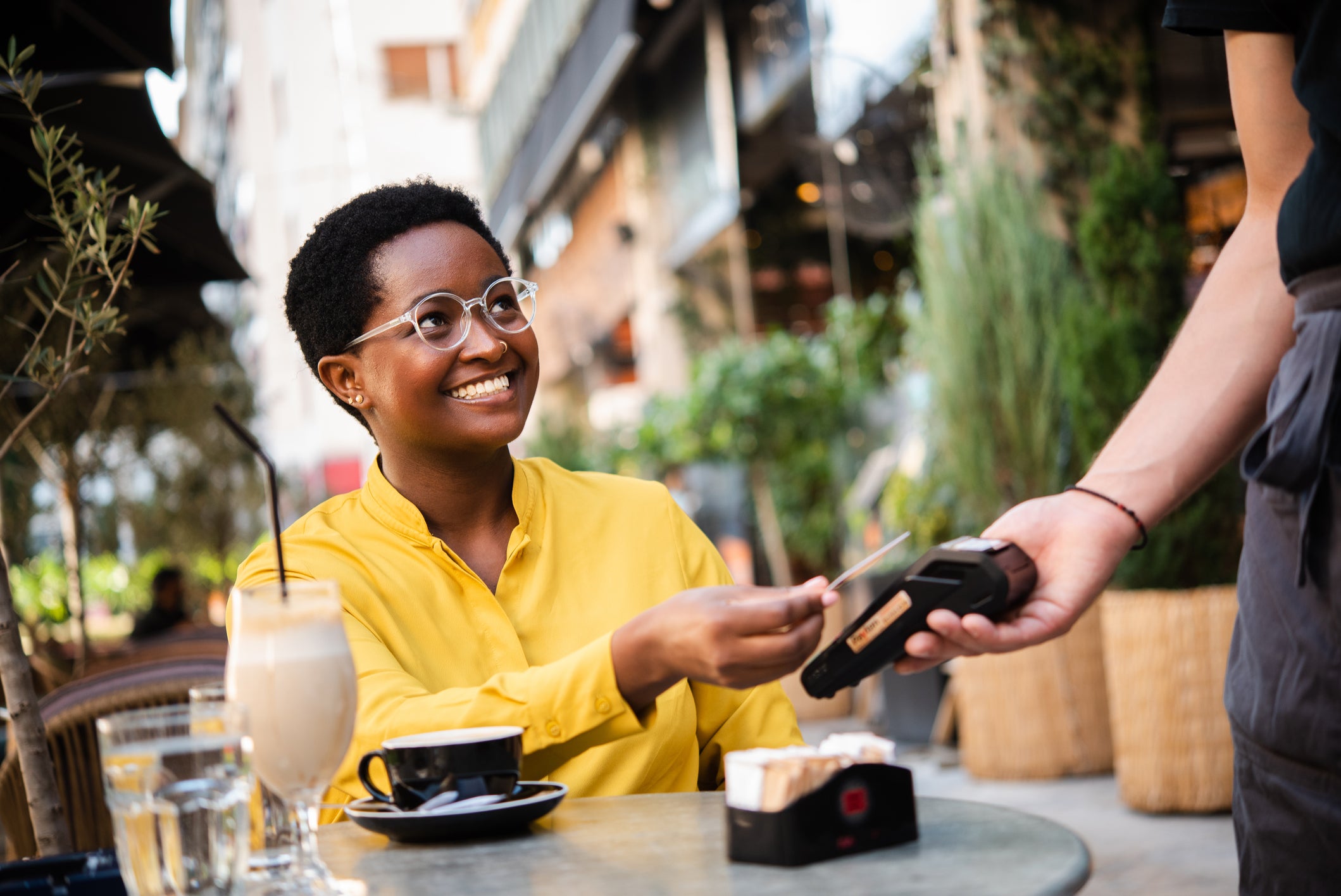 Young African American woman woman sitting at the cafe and paying for her coffee with a credit card