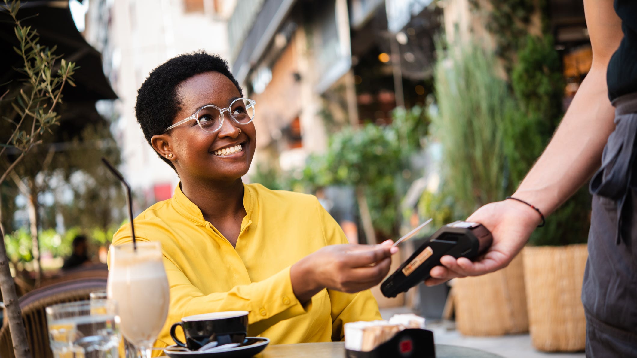 Young African American woman woman sitting at the cafe and paying for her coffee with a credit card