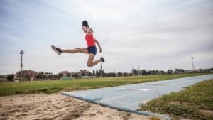 A young woman long jumps at a sports facility.