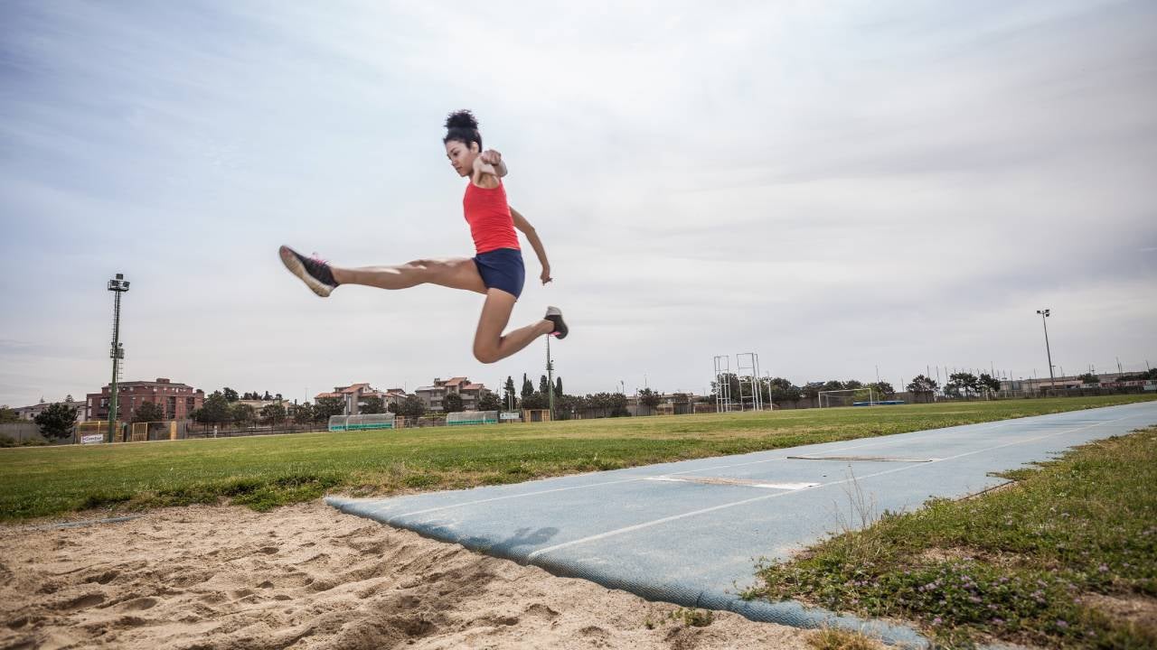 A young woman long jumps at a sports facility.