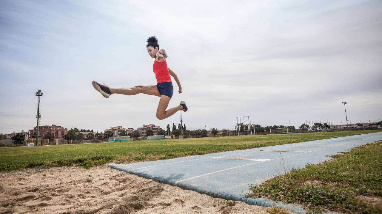 A young woman long jumps at a sports facility.