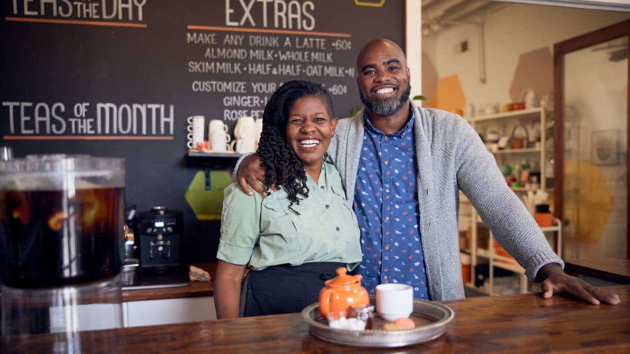 Owners of a tea shop pose behind the counter of their store.