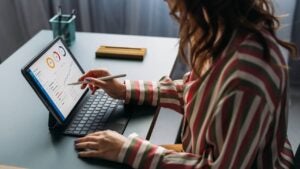 Focused young female analyzing financial statistics on digital tablet, working from a modern home office setup.