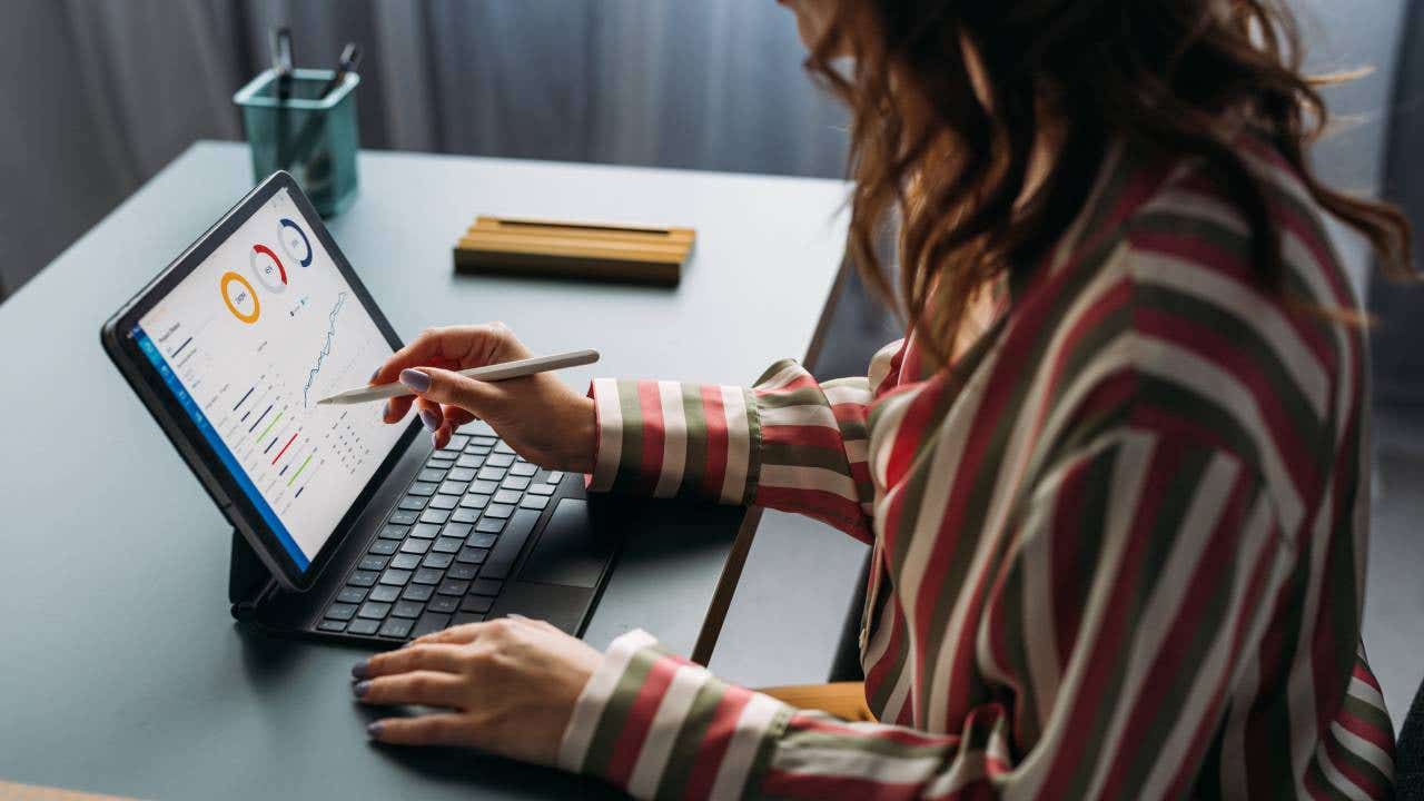 Focused young female analyzing financial statistics on digital tablet, working from a modern home office setup.