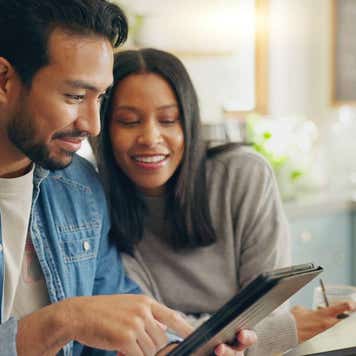 A couple works on a laptop and a tablet in their home.